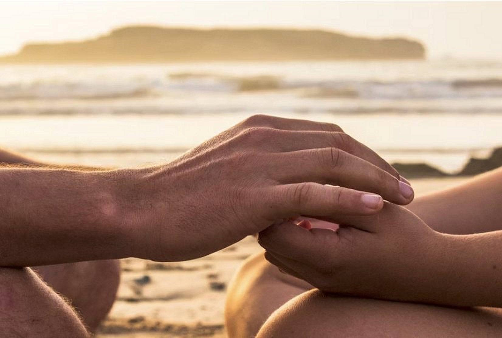 Two hands resting together on a beach at sunset
